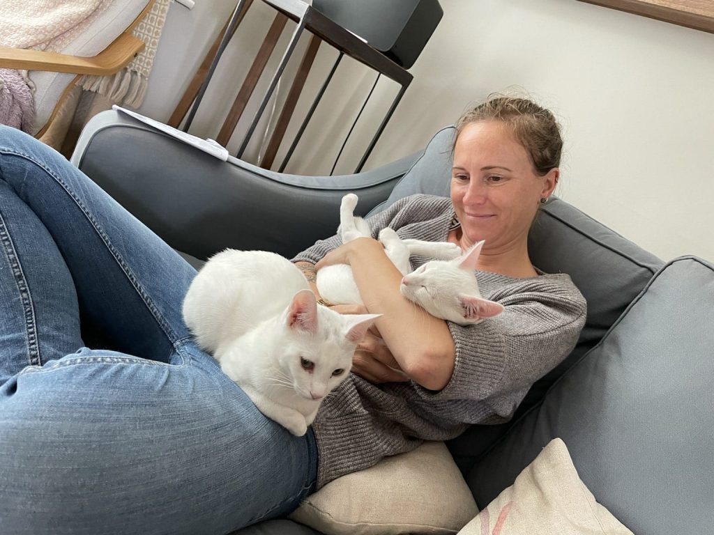 Ruth sitting,cuddling two white cats.